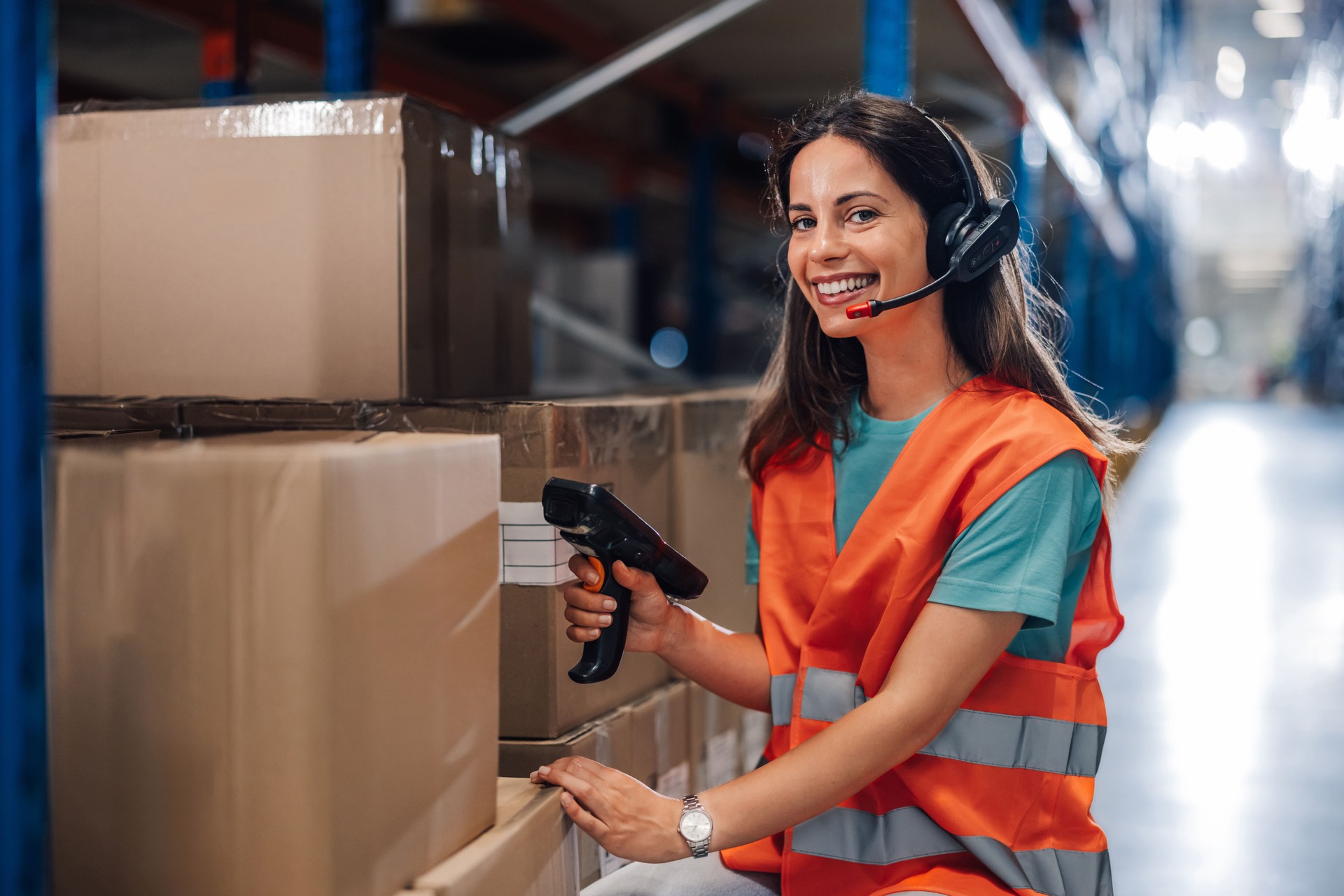 Female warehouse worker scanning barcodes on boxes and using headset